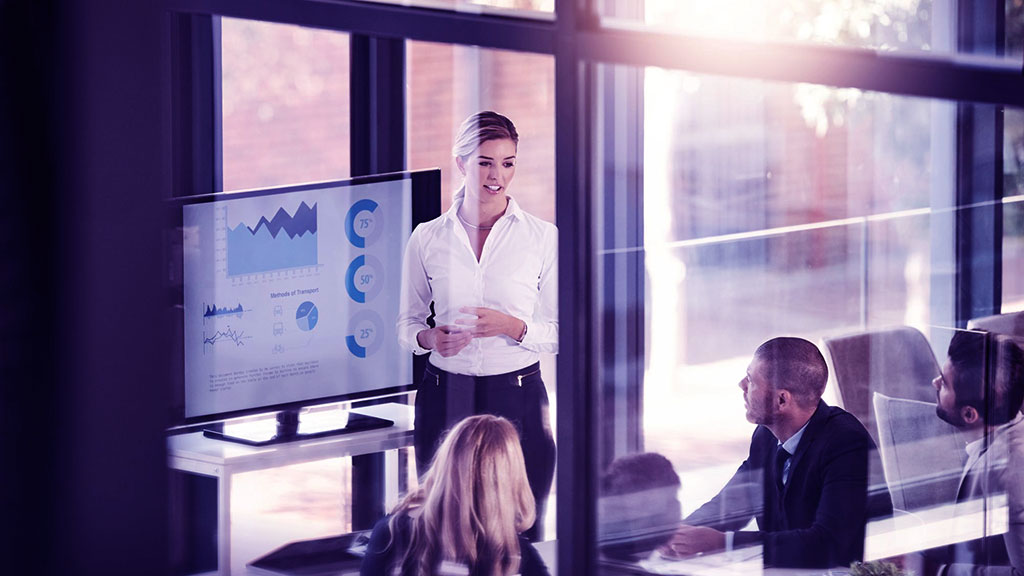 "Líder de proyectos presentando un tablero de control con gráficos de avance ante su equipo en una sala iluminada, ilustrando por qué monitorear proyectos genera mejores resultados."