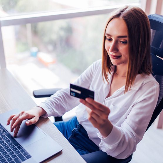 Compradora validando una transacción segura en comercio electrónico utilizando su tarjeta bancaria frente a la laptop