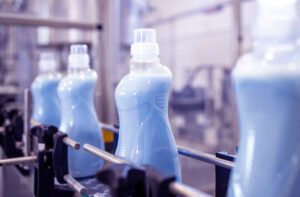 Botellas de detergente líquido azul avanzando en una cinta transportadora industrial automatizada.