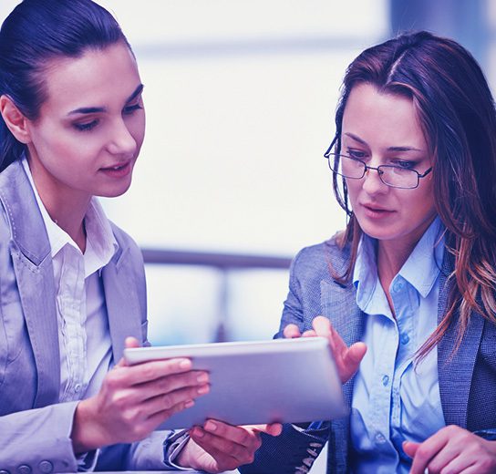 Consultora experta revisando una estrategia digital en una tablet junto a una ejecutiva en una oficina